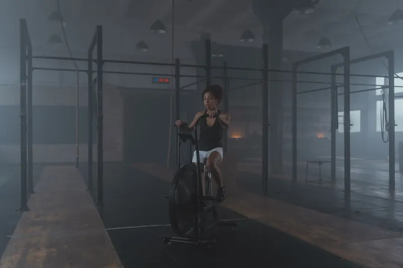 A woman works out on a stationary bike in a dimly lit gym setting, promoting fitness and healthy living