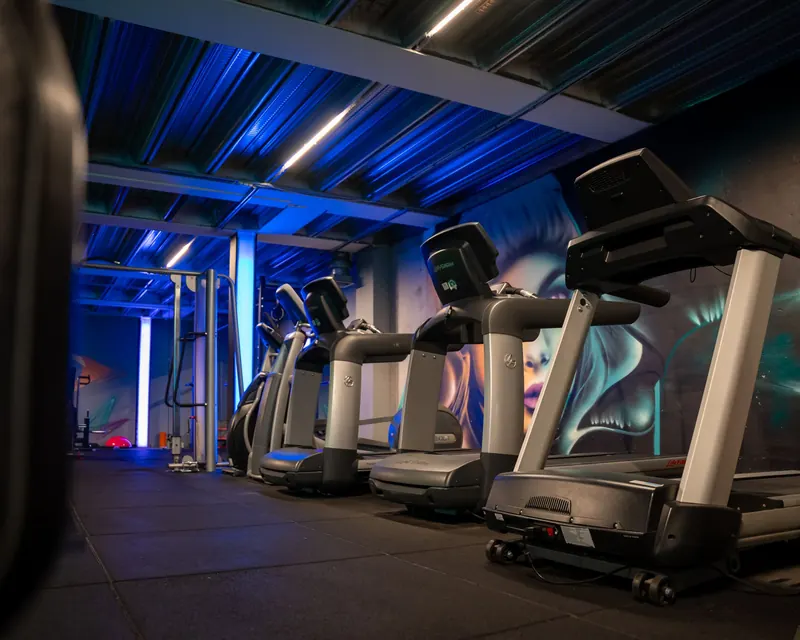 A sleek gym showcasing multiple treadmills with modern blue neon lighting and wall art