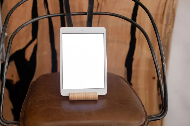 A digital tablet with blank screen on a metal chair with leather seat indoors