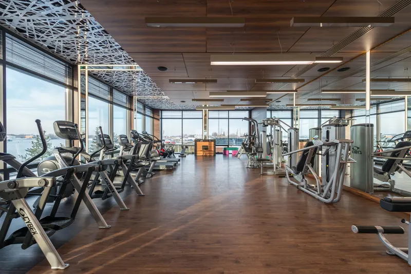 Interior of modern spacious fitness club with various sports machines and equipment placed on parquet floor near panoramic windows