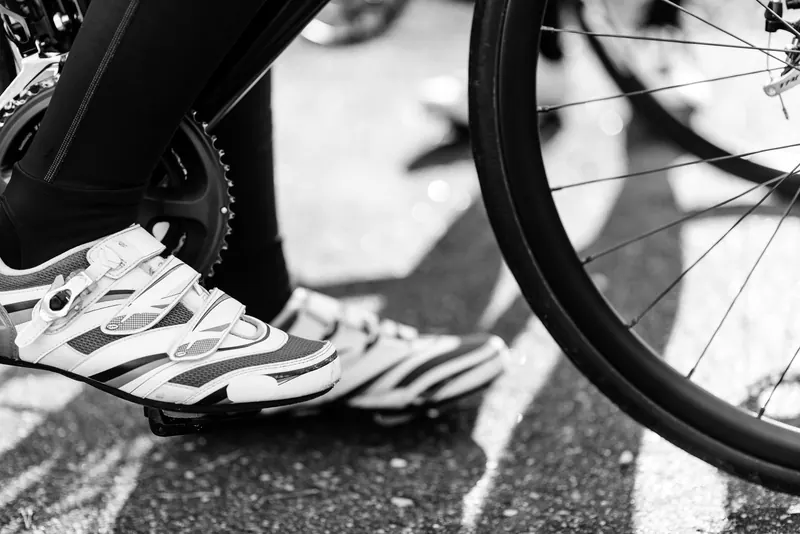 Black and white image showing a cyclist's feet with cleats on a bike pedal, capturing motion and detail